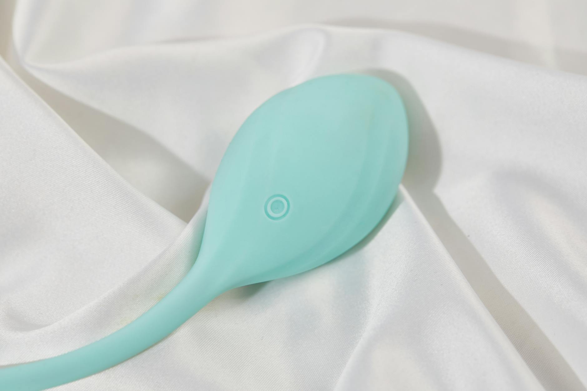 A sleek teal vibrator resting on white silk, symbolizing elegant self-care and sustained pleasure