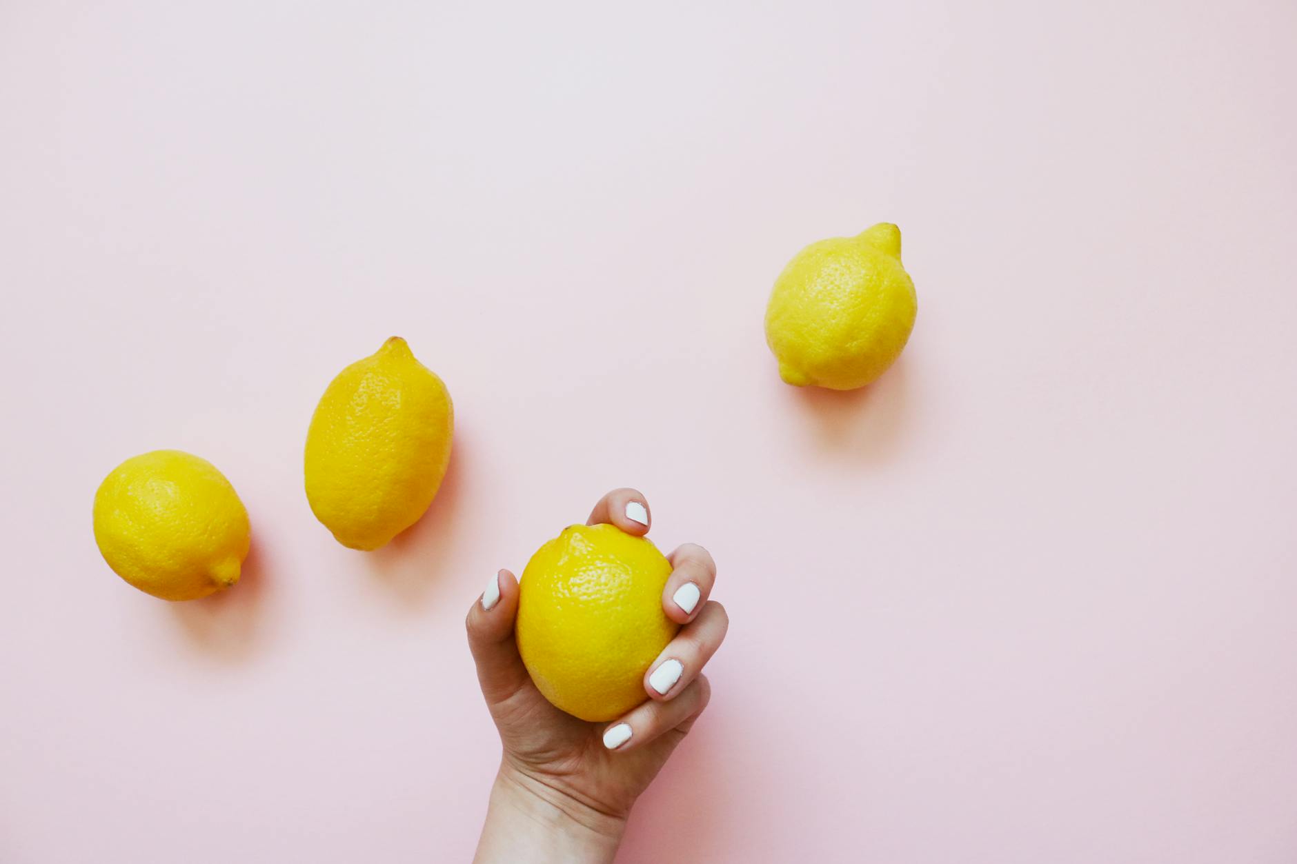 A hand holding a fresh lemon on a soft pink background with additional lemons nearby, symbolizing the suction technology in lemon clitoral vibrators.