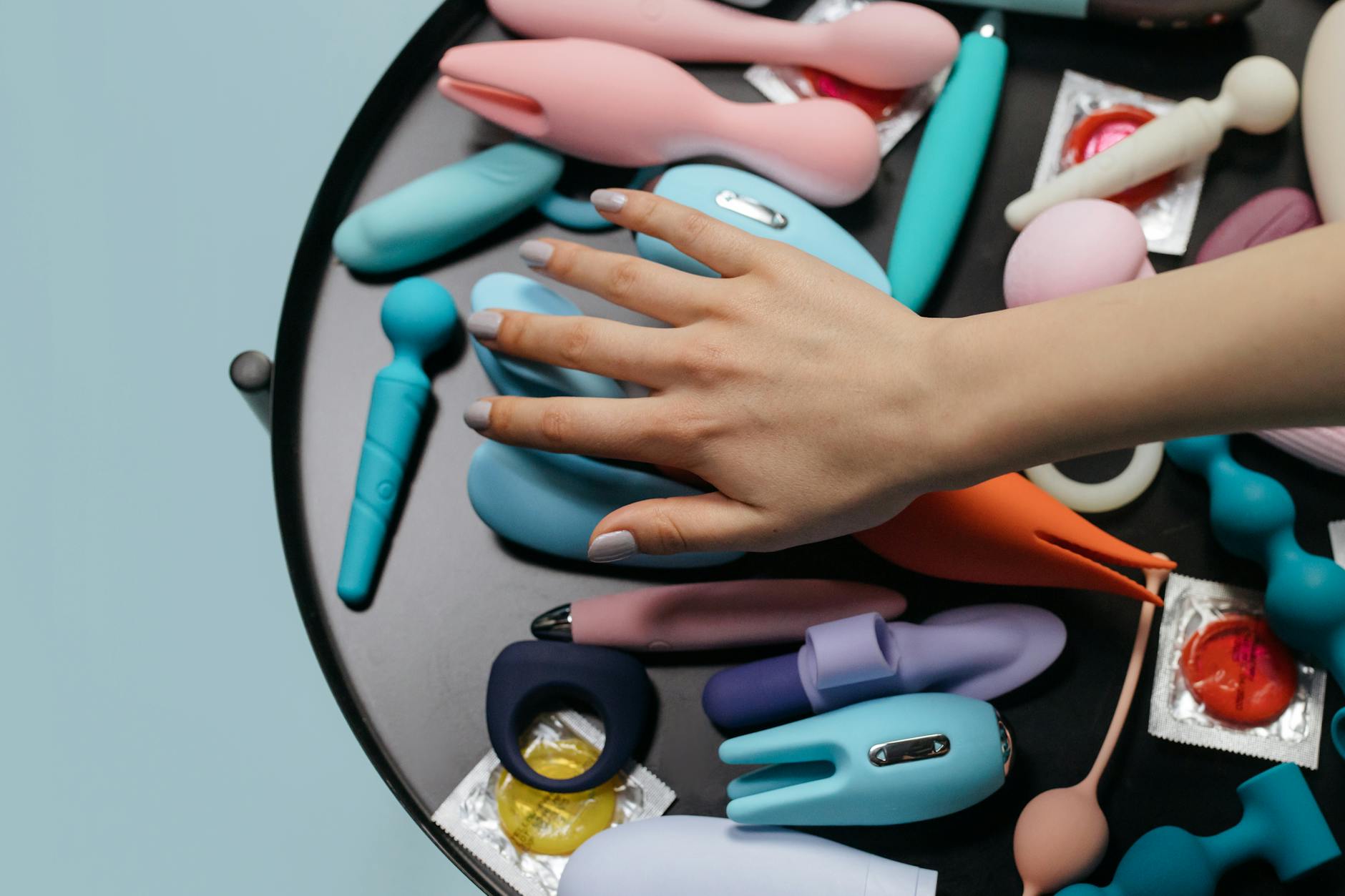 Woman holding blue and pink silicone vibrators in a contemplative manner