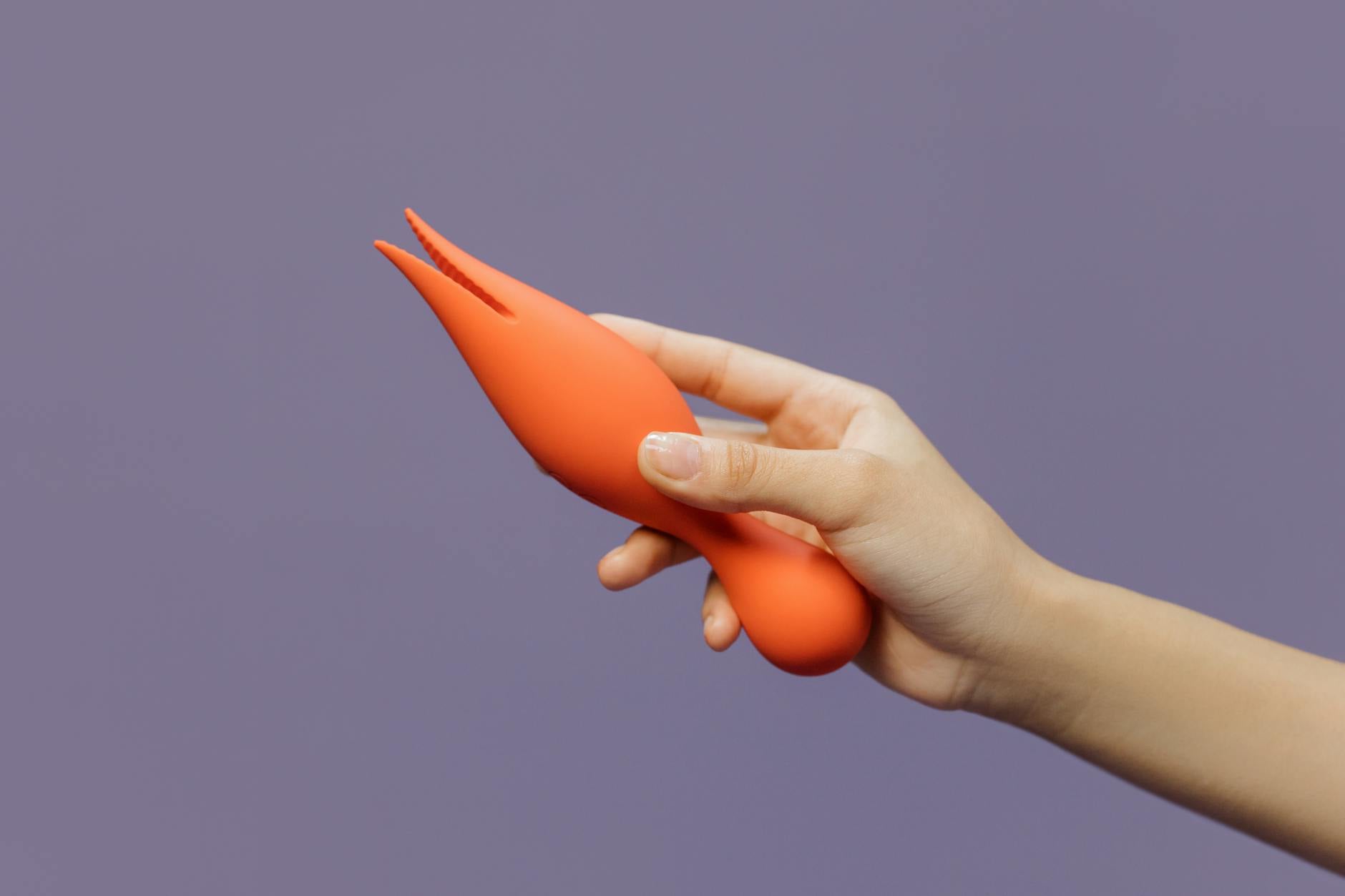 A hand holding a modern clitoral vibrator against a purple backdrop, showcasing mindful pleasure design.