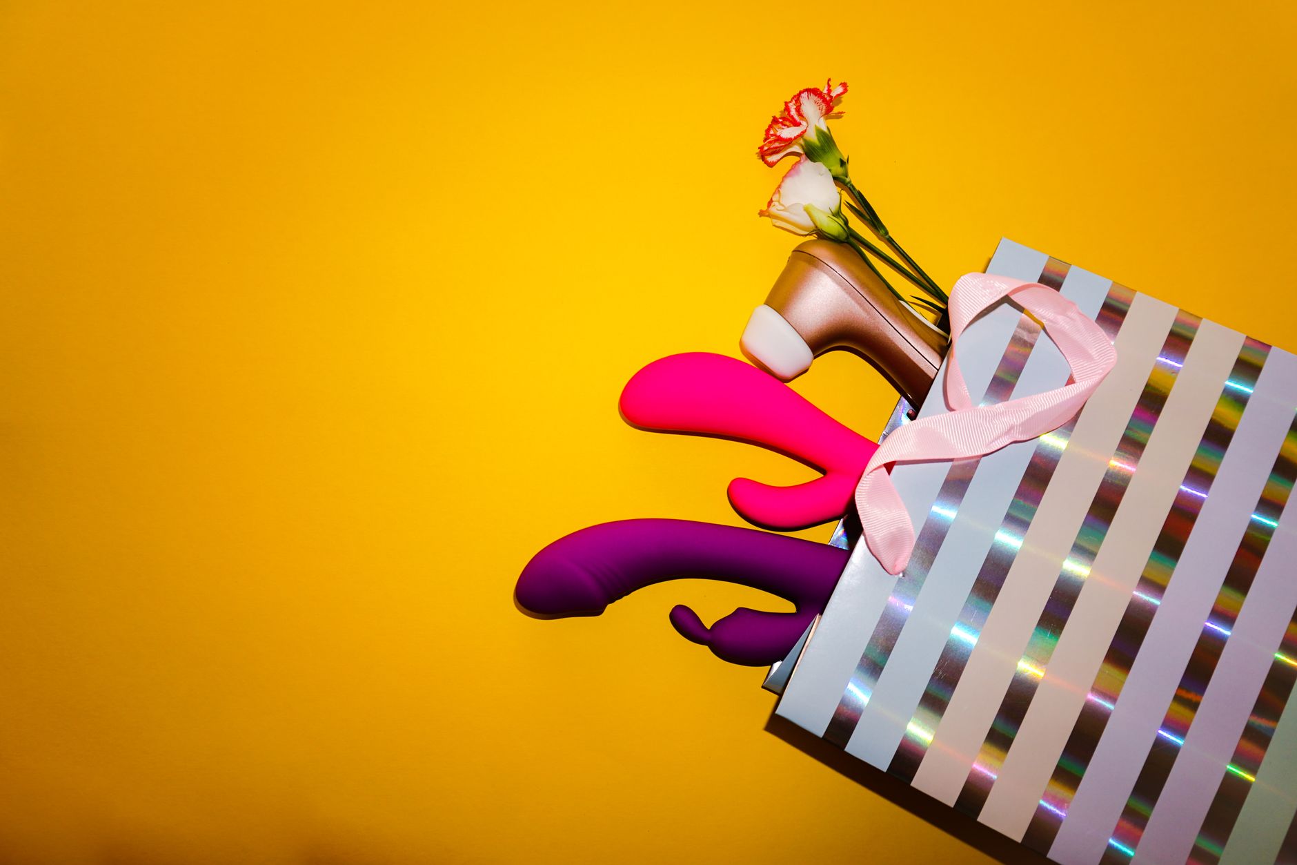 Collection of colorful lemon vibrators and toys displayed in a holographic gift bag against a bright yellow background